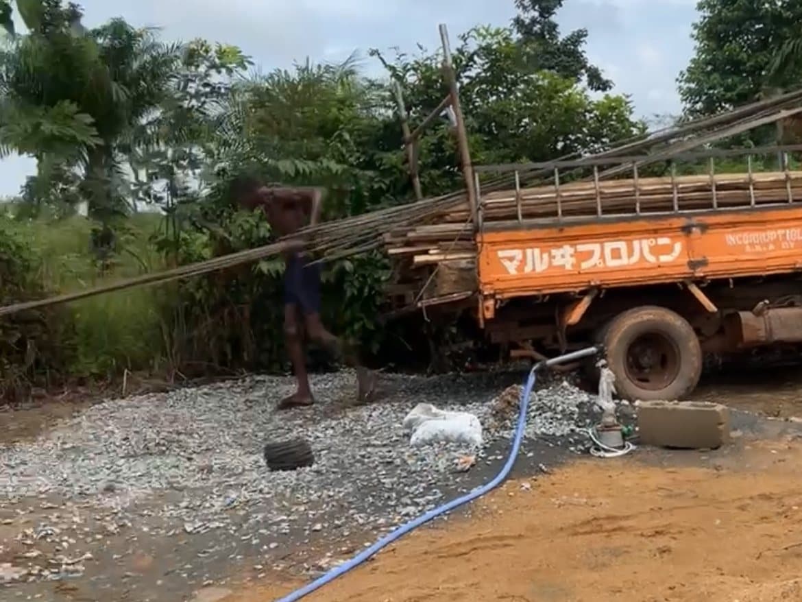 A man working on a pile of gravel beside a loaded truck.